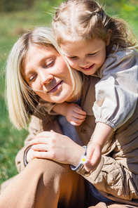 little child holding blurred flower near happy mom outdoors
