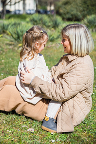side view of mother and child smiling at each other while sitting on lawn in park
