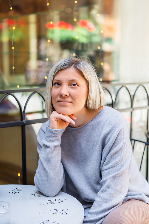 happy blonde woman looking at camera while sitting in street cafe