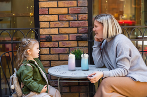 side view of excited woman sitting near daughter and glasses with milkshake in street cafe
