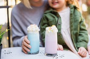 cropped view of blurred mother and daughter near glasses with milkshake and whipped cream