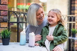 pleased girl touching belly near glasses with delicious milkshake and mom