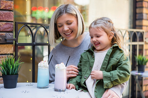 smiling girl looking at delicious milk dessert near happy mother in street cafe