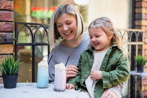 smiling girl looking at delicious milk dessert near happy mother in street cafe