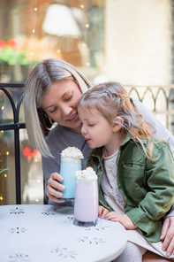 little child enjoying delicious milkshake near mom in cafe outdoors