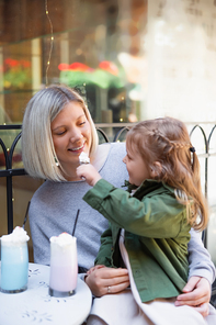 little child feeding happy mother with whipped cream in cafe on city street