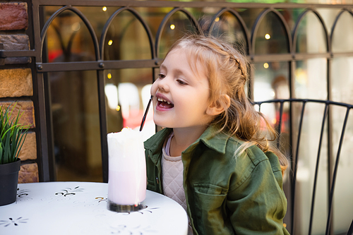 happy child reaching straw in glass of tasty milkshake outdoors