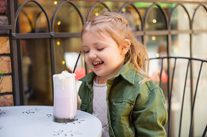 cheerful girl sitting near milkshake while sitting outdoors