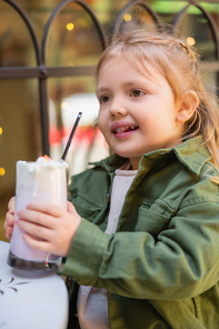 happy girl holding glass with milkshake on blurred foreground