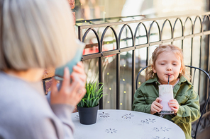 girl with closed eyes enjoying delicious dessert near blurred mom in cafe on street