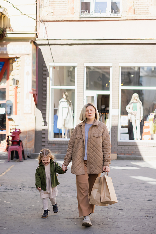 full length view of woman with shopping bags holding hands with happy daughter while walking outdoors