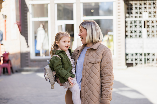 amazed blonde woman holding little daughter on city street