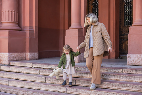 mother and daughter with teddy bear walking on stairs outdoors