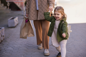 excited child holding hands with mom walking with shopping bags outdoors