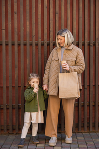 little girl drinking coffee from paper cup near mom with shopping bag