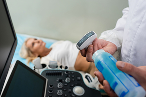 doctor applying ultrasonic gel on ultrasound probe near patient lying on blurred background