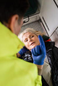 High angle view of blurred paramedic showing finger while giving first aid to mature woman in emergency vehicle