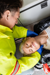 Top view of paramedic in latex gloves checking neck of middle aged woman in emergency vehicle