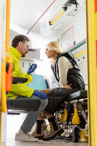 Side view of paramedic in latex gloves talking to mature patient in emergency car