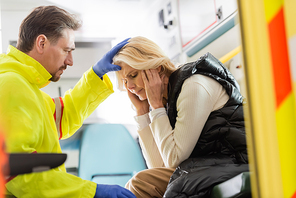 Paramedic in latex gloves touching head of middle aged woman in emergency car