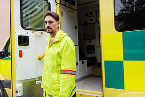 Paramedic in uniform standing near ambulance car on urban street