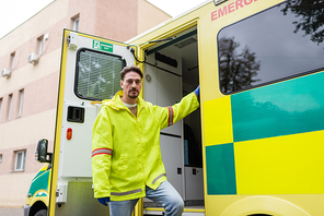 Paramedic in latex gloves and jacket looking at camera near ambulance car outdoors