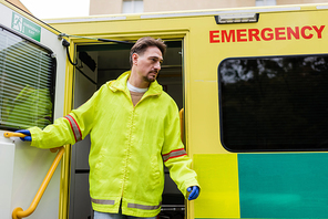 Paramedic in latex gloves and jacket opening door of ambulance vehicle outdoors