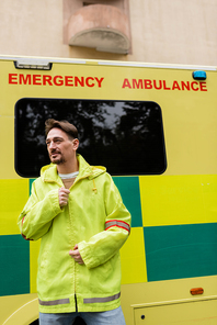 Paramedic wearing jacket near ambulance car on urban street