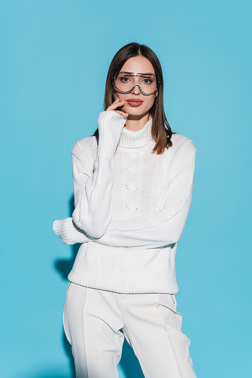 pretty young woman in eyeglasses and white turtleneck looking at camera on blue