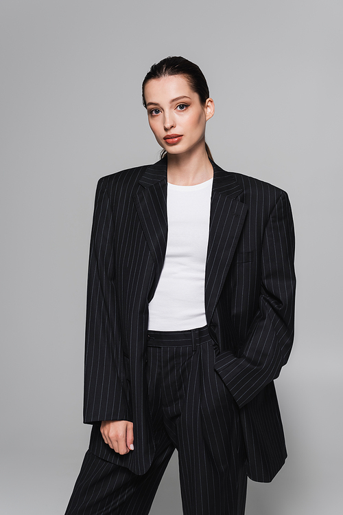 Trendy young woman in black suit posing with hand in pocket isolated on grey