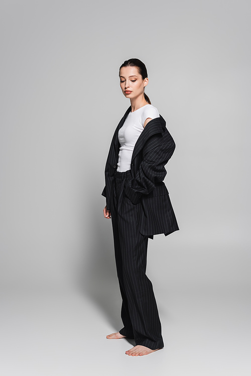 Full length of fashionable woman in suit standing on grey background