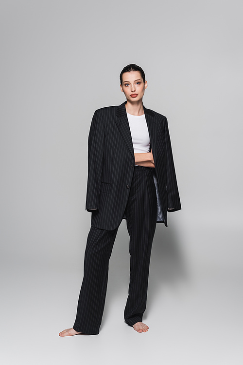 Full length of barefoot model in suit posing on grey background
