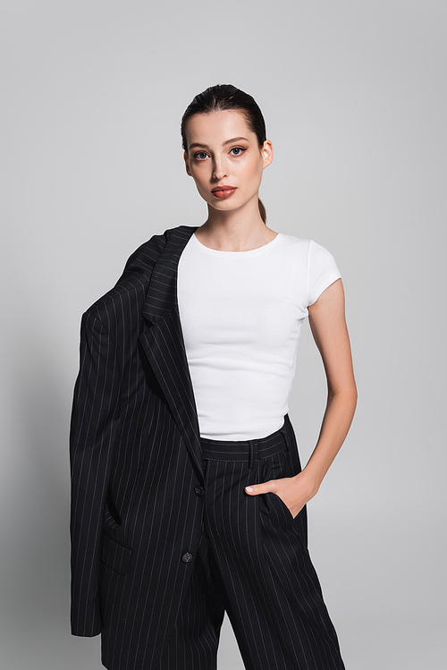 Stylish woman in t-shirt and striped suit posing on grey background