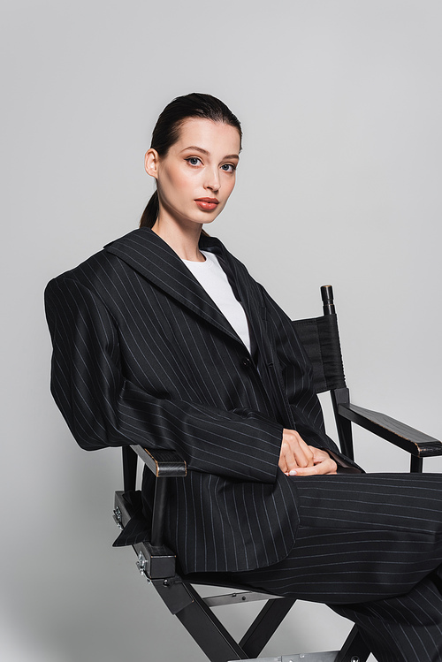 Stylish woman in suit sitting on folding chair on grey background
