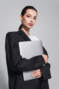 Portrait of young woman in striped jacket holding laptop isolated on grey