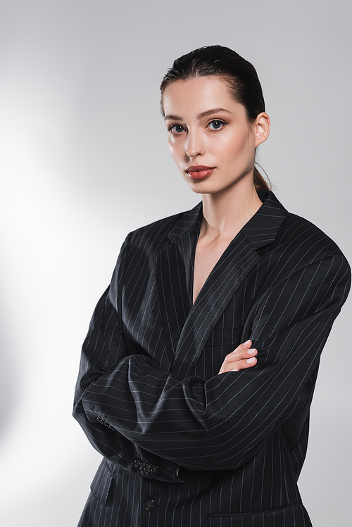 Fashionable woman in black jacket crossing arms on abstract grey background