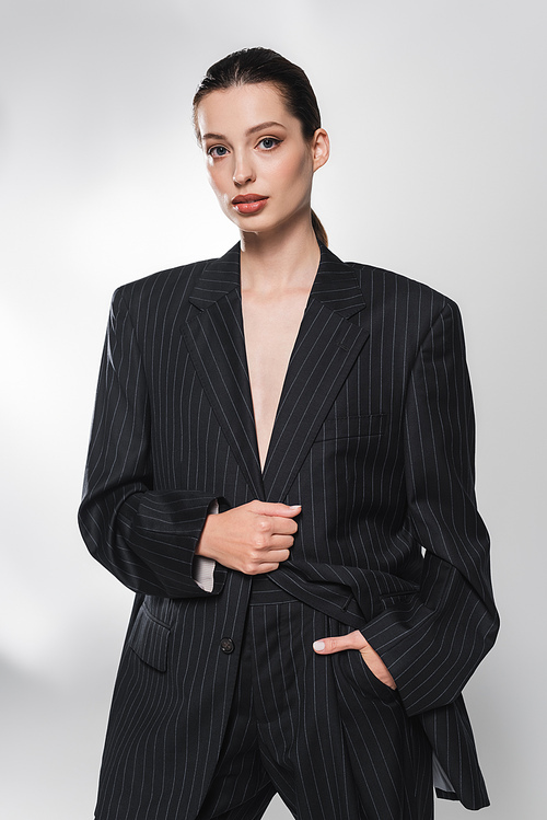 Portrait of trendy model in suit holding hand in pocket on grey background