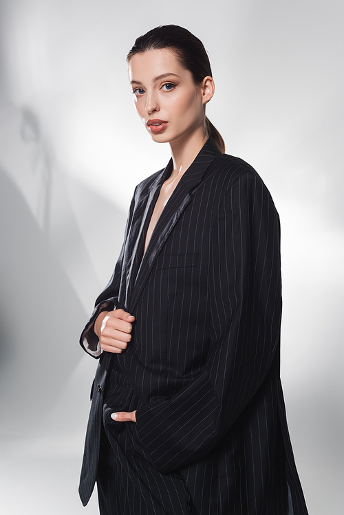 Stylish model in striped suit looking at camera on abstract grey background