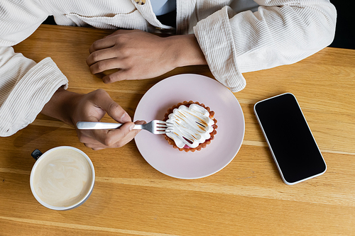 top view of african american man holding fork near tasty tart and smartphone with blank screen