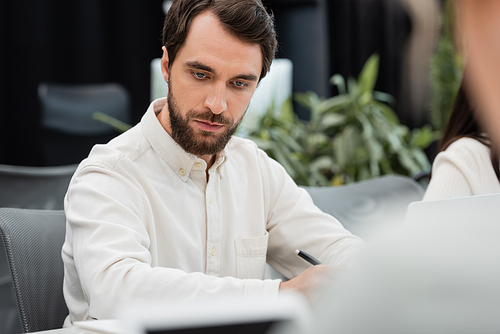serious bearded businessman working in office on blurred foreground