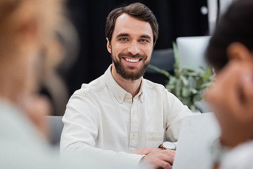 bearded businessman looking at camera in office on blurred foreground