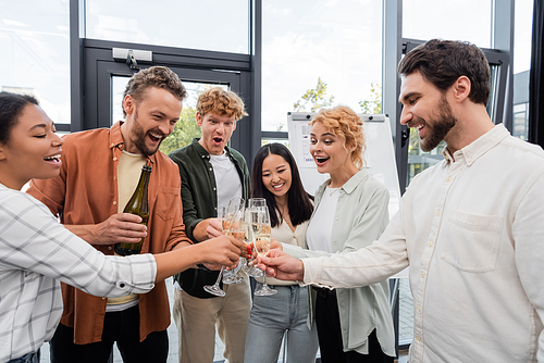 excited multiethnic business people clinking champagne glasses during corporate party in office