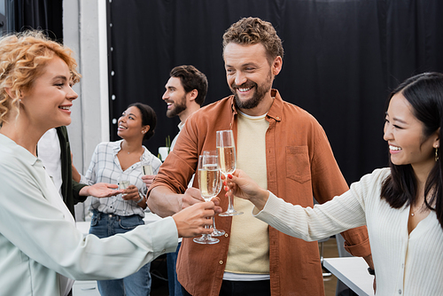 Cheerful interracial business people toasting and holding champagne in office