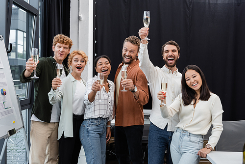 Excited multicultural business people rising glasses of champagne in office