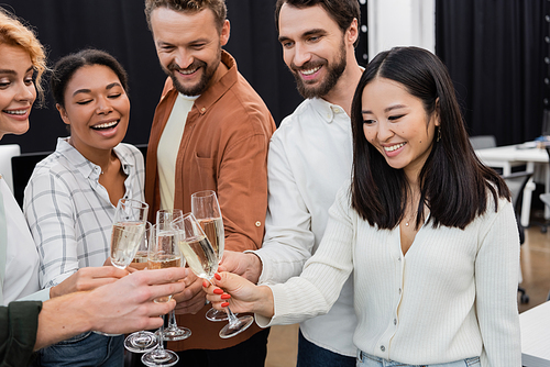 Smiling asian businesswoman clinking champagne with multiethnic colleagues in office