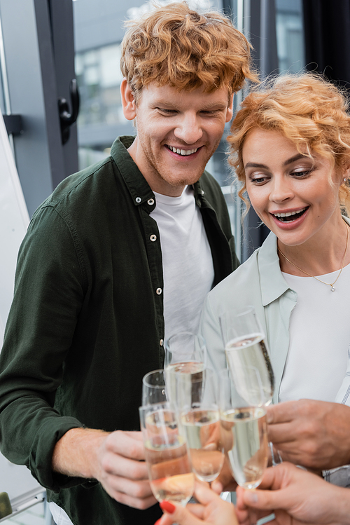Smiling redhead businessman in casual clothes clinking champagne with colleagues in office