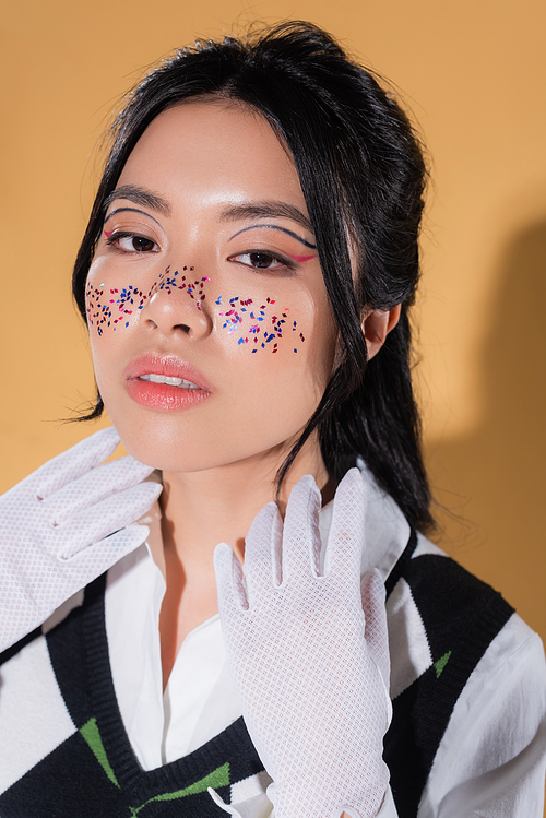 Fashionable asian model with glitter on face looking at camera on orange background