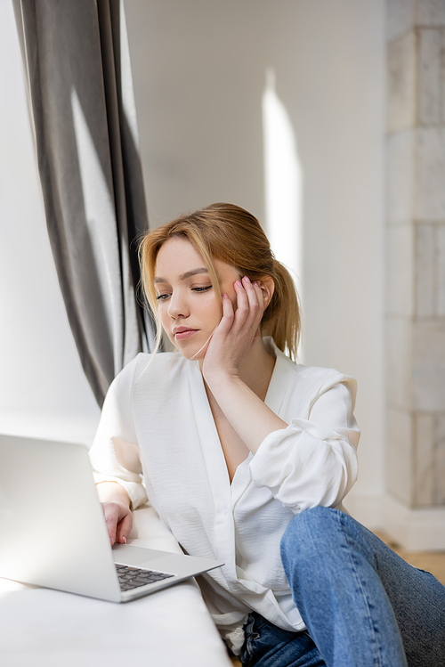 Blonde freelancer using blurred laptop at home