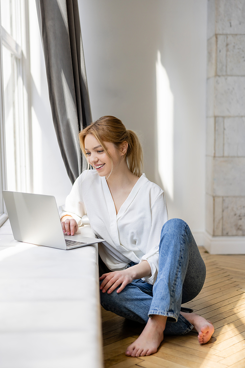 Smiling freelancer using laptop on windowsill at home