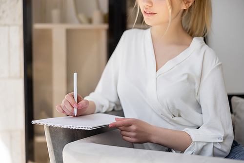 Cropped view of young woman in blouse writing on notebook on armchair